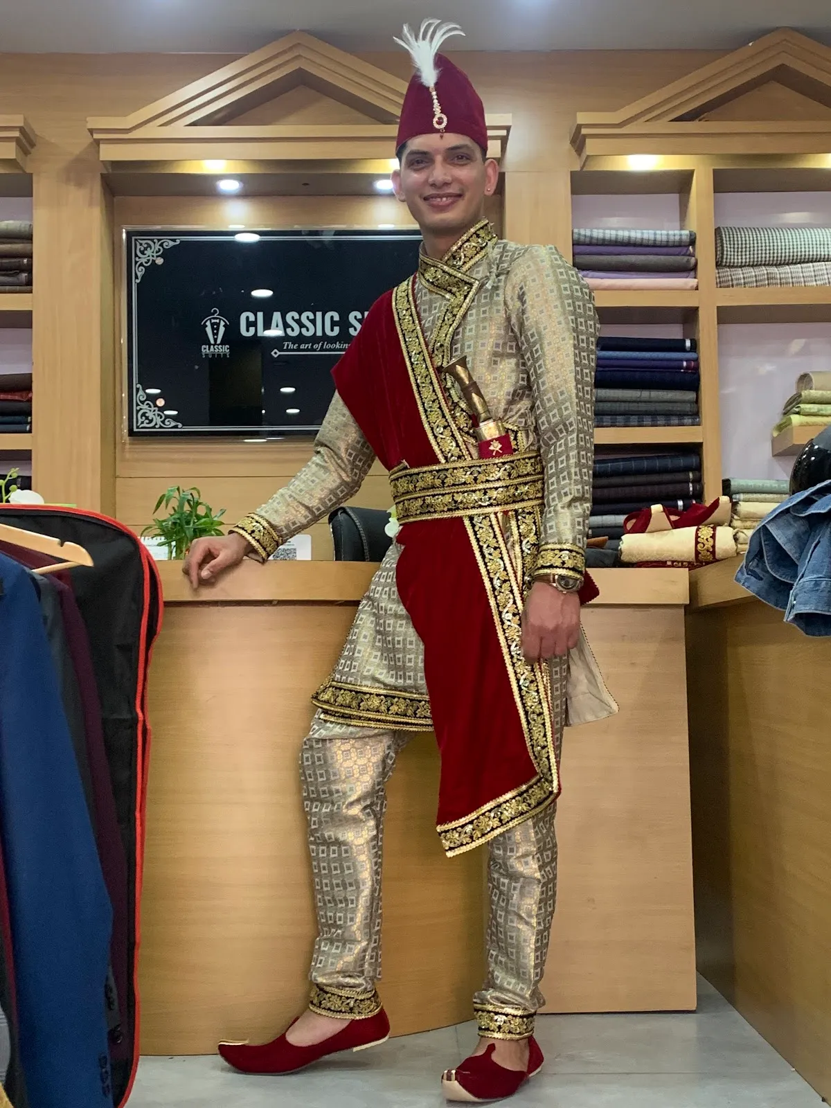 A gold-brocade sherwani with embroidered red and gold sash — heavy occasion wear.