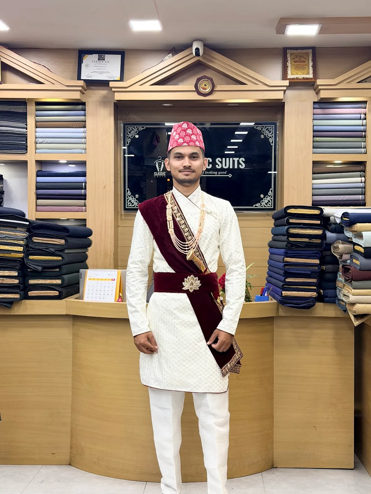 A cream-and-maroon wedding sherwani with embroidered velvet sash and matching trousers, tailored for a Pokhara wedding.